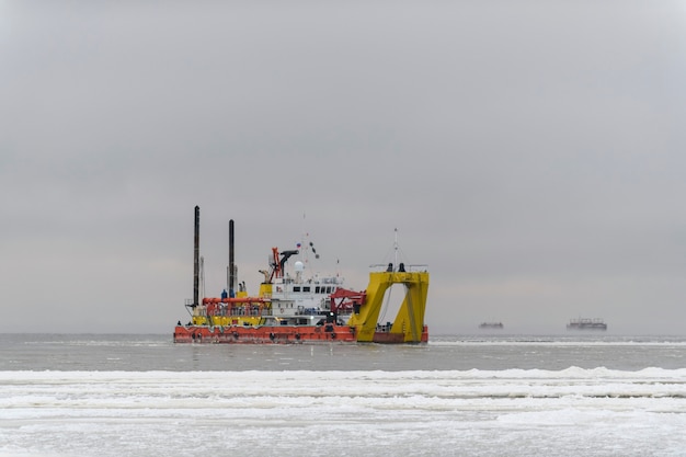 Schip bezig met baggeren bij zonsondergang. Hopperzuiger die op zee werkt. Schip dat materiaal uit een wateromgeving opgraaft.