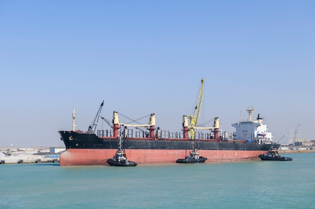 Schip nadert zijn ligplaats met sleepbootassistentie. Afmeren operaties. Bulker. Droog vrachtschip.