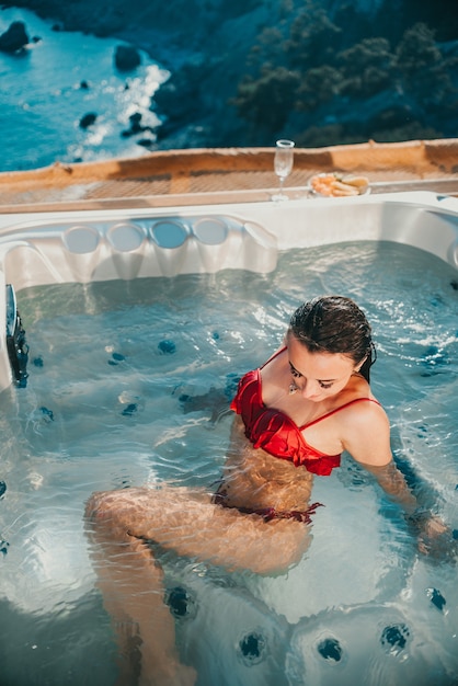 Schitterend meisje in een buitenjacuzzi met een prachtig uitzicht op de zee en de bergen