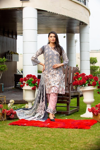 Schitterend meisje poseert met bloemen in de tuin en draagt trendy Shalwar Kameez voor modefotoshoot