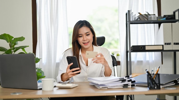 Schitterende Aziatische zakenvrouw die een applicatie voor mobiel bankieren gebruikt om haar winkelrekeningen te betalen