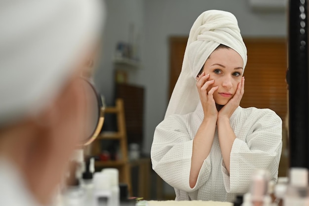 Schitterende blanke vrouw met handdoek op hoofd die voedende crème aanbrengt en dagelijkse schoonheidsroutine thuis maakt