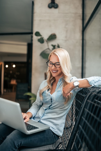 Foto schitterende blonde vrouw die laptop binnen met behulp van.