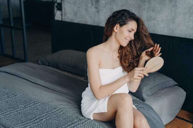 Schitterende Europese vrouw kamt haar lange zijdeachtige haar in slaapkamer Vrouwelijkheid en schoonheidsconcept