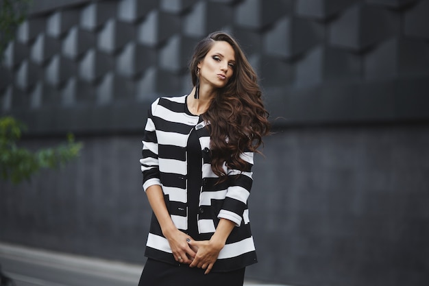 Schitterende jonge modelvrouw met perfect donker haar die zwarte avondjurk en jasje draagt die ...