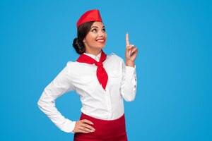 Schitterende jonge stewardess in rood en wit uniform die omhoog wijst en glimlacht