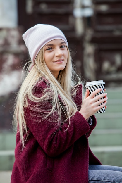 Schitterende jonge vrouw met kop koffie in stadsstraat