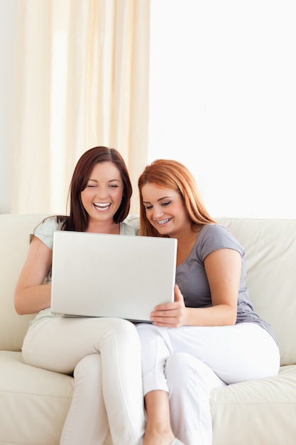 Schitterende jonge vrouwen die op een bank met laptop zitten