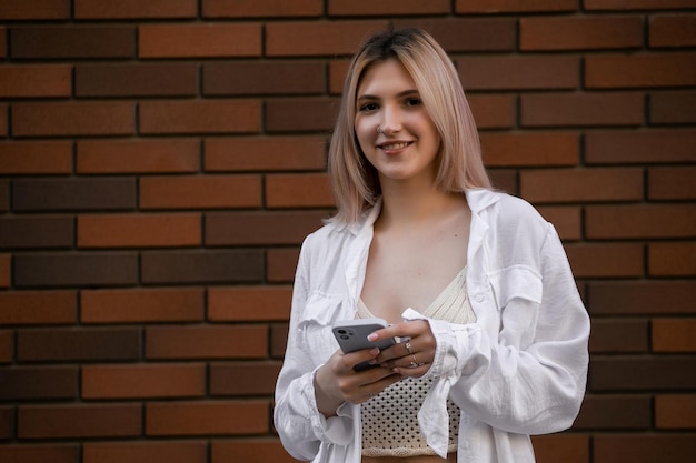Schitterende mooie jonge vrouw met blonde haarberichten op de smartphone op de achtergrond van de stadsstraat, mooi meisje dat een smartphonegesprek heeft op de stadsstraat