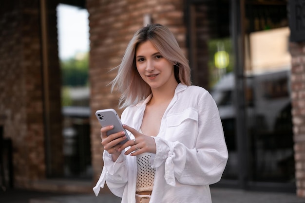 Foto schitterende mooie jonge vrouw met blonde haarberichten op de smartphone op de achtergrond van de stadsstraat, mooi meisje dat een smartphonegesprek heeft op de stadsstraat