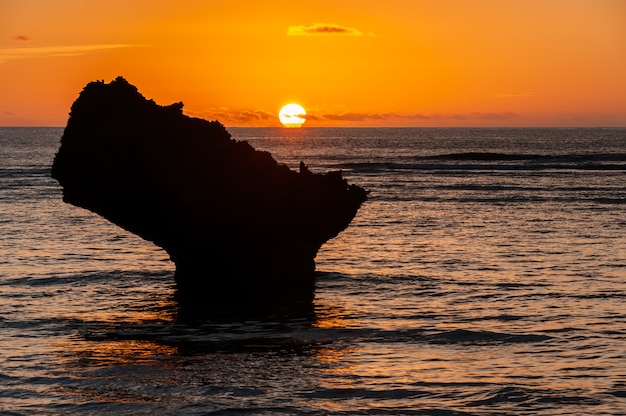 Schitterende oranje zonsondergang die aan de horizon achter een kustrots naar beneden gaat