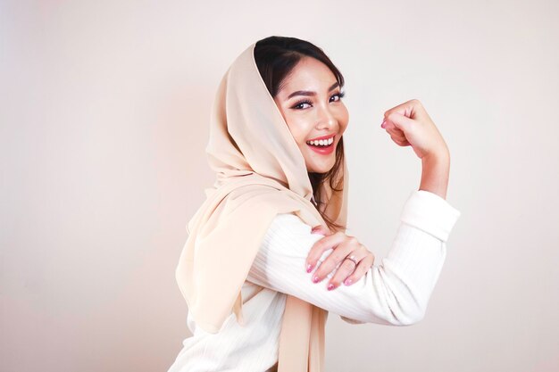 Schitterende sterke jonge moslimvrouw die over witte muur wordt geïsoleerd als achtergrond die biceps toont