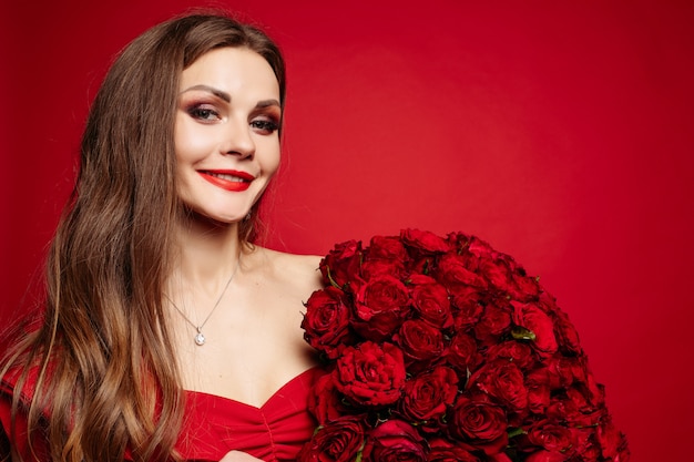 Schitterende vrouw in rode kleding die boeket van rozen houdt