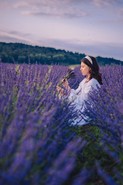 Schitterende vrouw in witte jurk bij zonsondergang in het lavendelveld