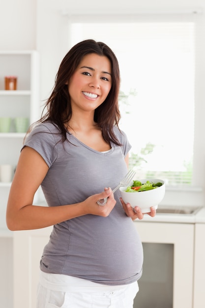 Schitterende zwangere vrouw die een kom salade houdt terwijl status