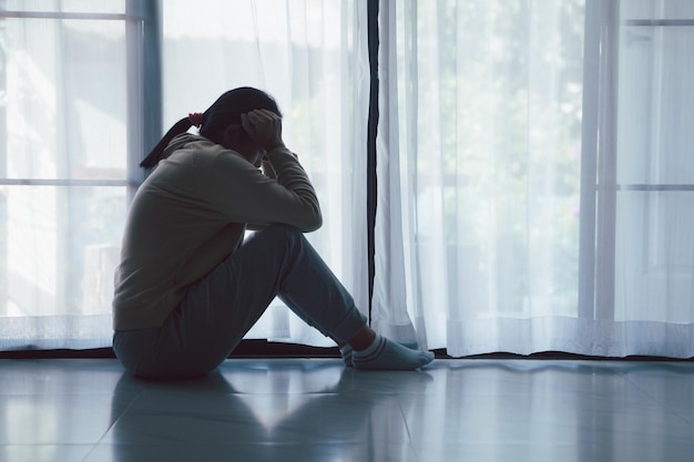Schizofrenie met eenzaam en verdrietig in de geestelijke gezondheid depressie concept Depressieve vrouw die thuis tegen de vloer zit met een donkere kamer die zich ellendig voelt Vrouwen zijn depressief, angstig en ongelukkig
