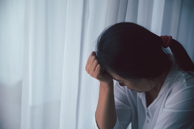 Schizofrenie met eenzaam en verdrietig in de geestelijke gezondheid depressie concept Depressieve vrouw die thuis tegen de vloer zit met een donkere kamer die zich ellendig voelt Vrouwen zijn depressief, angstig en ongelukkig