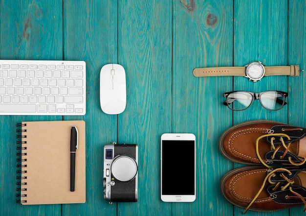 Schoenen camera smartphone notitieblok horloge bril toetsenbord en pc-muis op het blauwe houten bureau