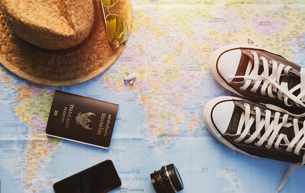 Schoenen, smartphone, lens, vliegtuig, strohoed en paspoort op kaart met zonlichteffect.