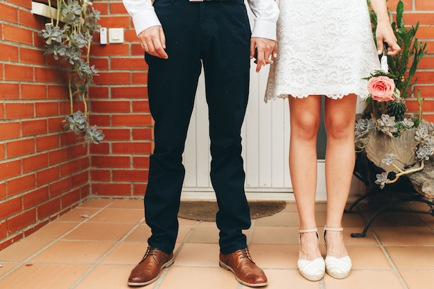 Schoenen van bruid en bruidegom en haar kleine bruiloft boeket van roze rozen met gevouwen handen na de ceremonie. Bruiloft concept. Trouwdag concept.