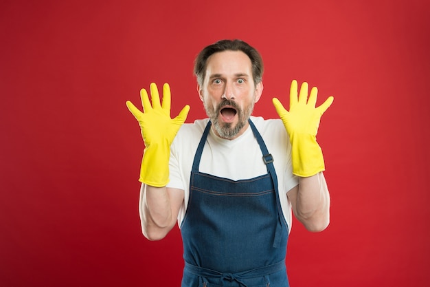 Schokkende resultaten. Op hun hoede voor netheid. Schoonmaakservice en huishoudelijke taken. Veel werk. Man in schort met handschoenen aan het schoonmaken. Vandaag schoonmaakdag. Bebaarde man die huis schoonmaakt. Bebaarde werknemer.