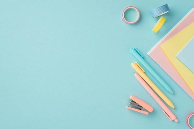 School accessories concept Top view photo of school supplies mini stapler adhesive tape colorful pens and copybooks on isolated pastel blue background with copyspace