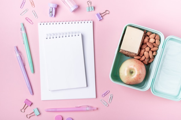 School achtergrond met laptops en pastel kleurrijke studie accessoires op roze achtergrond Lunch doos met appel, sandwich