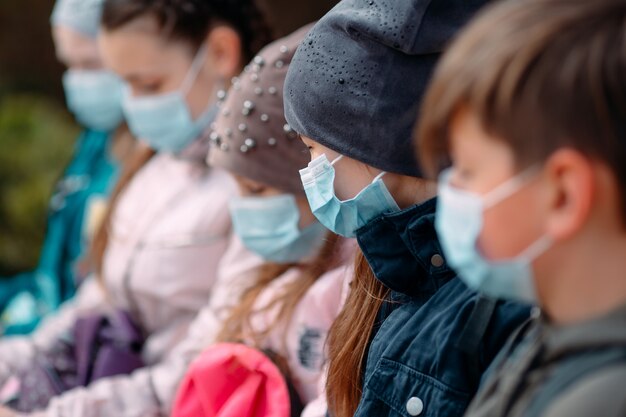 School-age children in medical masks sit on a bench.