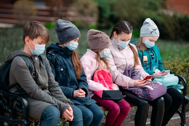 I bambini in età scolare in maschera medica siedono su una panchina.