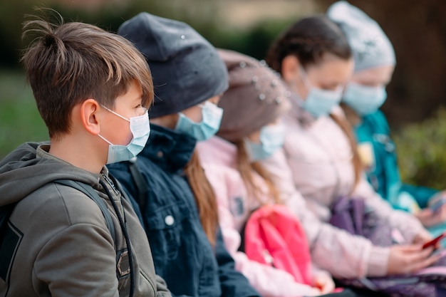 School-age children in medical masks sit on a bench.