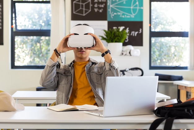 in school asian teenage boy using vr headset while studying with laptop and notebook
