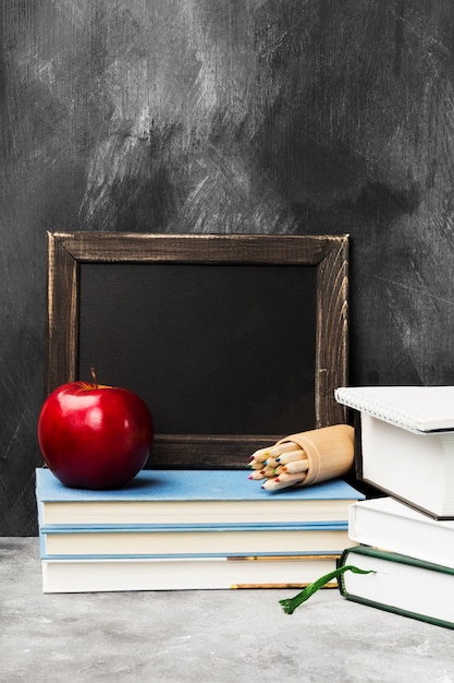 Photo school attributes - black board, books, colored pencils, notebook, apple on dark background. copy space