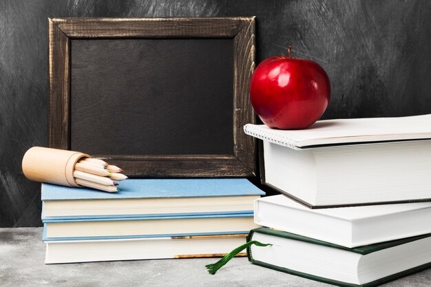 School attributes - black board, books, colored pencils, notebook, apple on dark background. Copy space