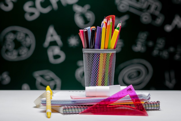 School background with stationery accessories. Books, globe, pencils and various office supplies lying on the desk on a green blackboard background