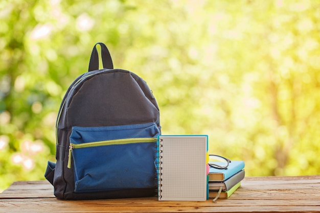 School backpack with books on wooden table and nature background