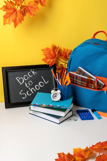 Foto zaino scuola con materiale scolastico colorato e lavagna con lettere di ritorno a scuola. forniture scolastiche su sfondo giallo. disegno del banner