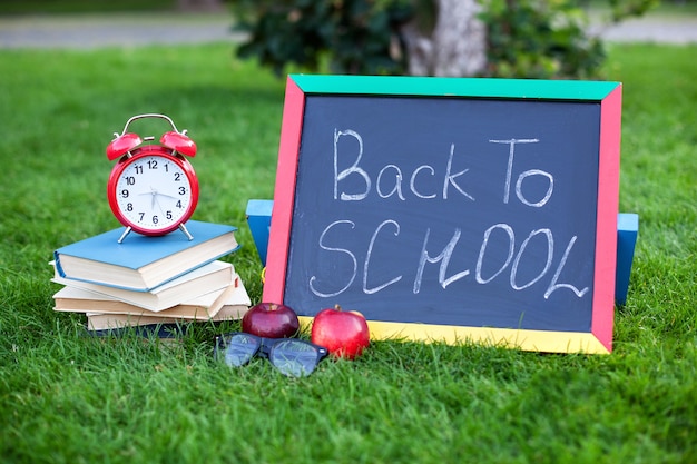 School books with red alarm clock and blackboard with back to school quote