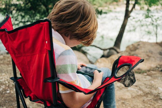 Photo school boy kid child playing texting with his cellphone mobile smartphone while sitting on the red