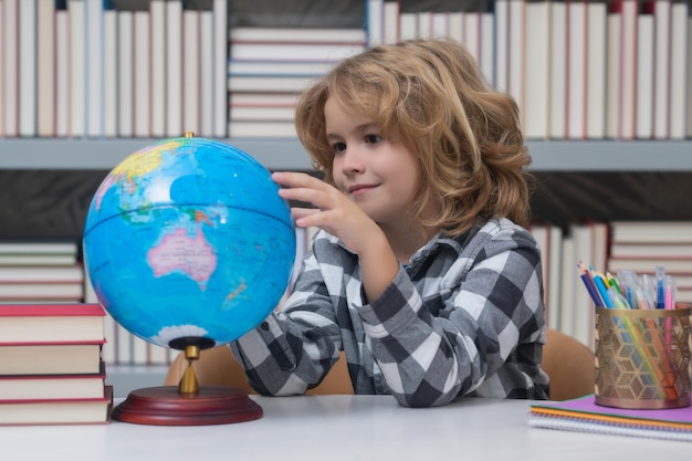Foto ragazzo di scuola che guarda il globo nella lezione di geografia della biblioteca studente scolastico che impara in classe studia lingua inglese a scuola bambino di scuola elementare ritratto divertente di apprendimento di un allievo