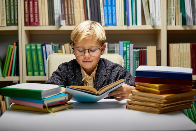 school boy reading book while preparing for lesson in library, diligent and shy child is concentrated on reading