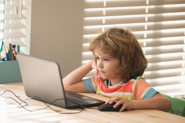 Photo school boy sitting at the table writing homework or preparing for the exam child using notebook comp
