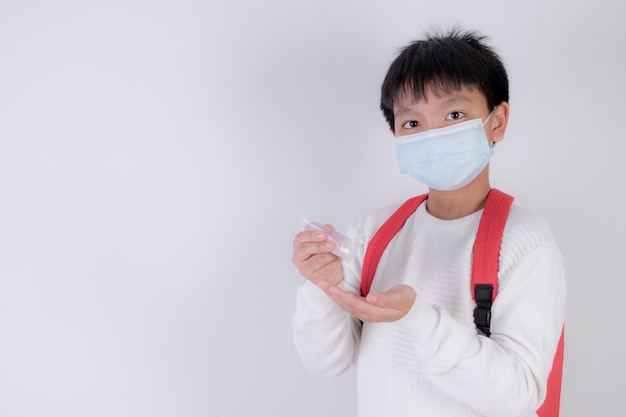 Photo school boy wearing face mask and applying hand sanitizer, school reopen after covid-19 pandemic.