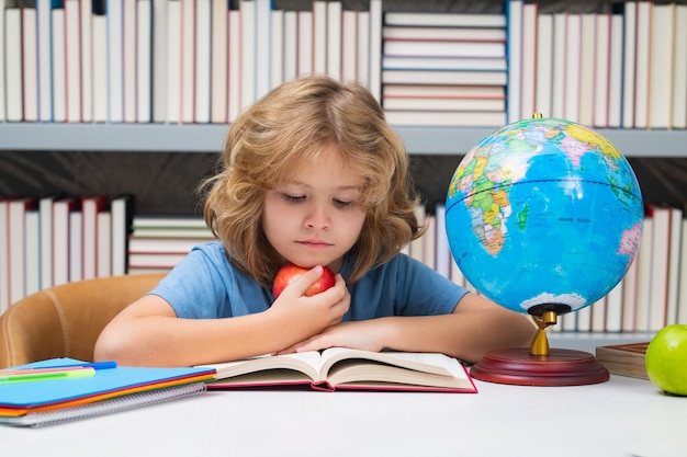 School boy with books and apple in library back to school funny little boy from elementary school wi