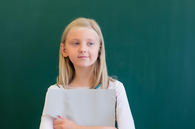 School child girl in classroom Funny kid against a green chalkboard Idea and creativity concept