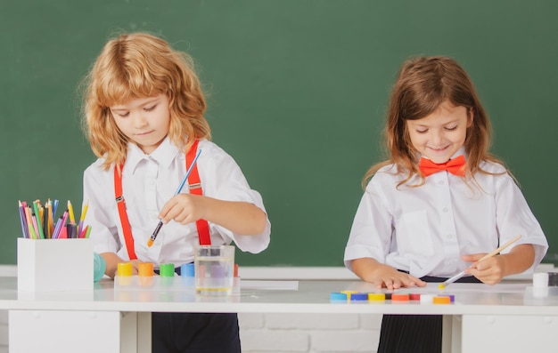 School children drawing a colorful pictures with pencil crayons in classroom on blackboard backgroun