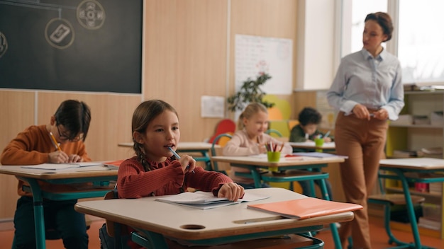 school class lesson children studying learning in classroom woman teacher female tutor walking teaching little boy child kid rise hand ask help question answer study learn write talking education