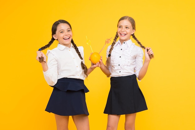 School dieet Basisschoolleerlingen drinken sap van oranje fruit op gele achtergrond Kleine kinderen genieten van gezonde schoolsnack Kleine meisjes met vitaminerijke drank in schooluniform
