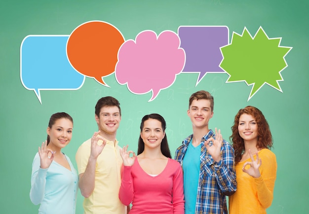 school, education, communication, gesture and people concept - group of smiling teenagers showing ok sign over green board background with text bubbles