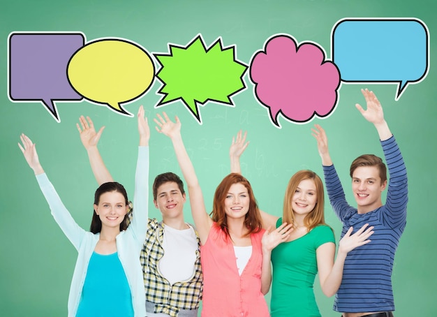 school, education, communication, gesture and people concept - group of smiling teenagers waving hands over green board background with text bubbles