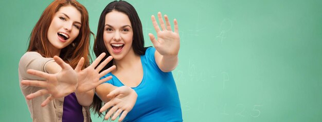 学校、教育、幸福、人々 のコンセプト - 緑のチョーク ボードの背景の上に手のひらを示す 2 つの笑顔の学生の女の子または若い女性